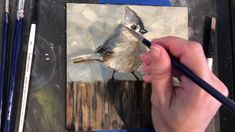 a person is painting a bird on a piece of wood with watercolor pencils