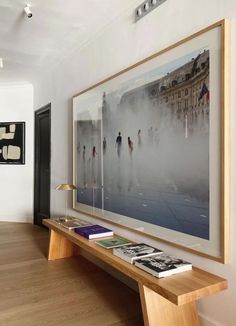 an art work hangs on the wall above a wooden table with books and magazines under it