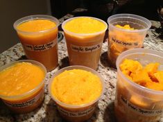 several plastic cups filled with food sitting on top of a marble counter covered in orange sauce