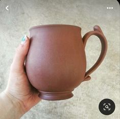 a person holding a brown mug in their right hand and the other hand is holding it up