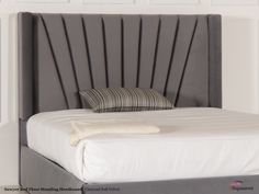 a white bed with a gray headboard and pillows on it's sides, in a bedroom