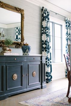 an image of a room with blue and white curtains on the window sill in front of a mirror