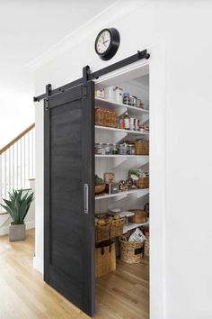 an open pantry door with shelves and baskets on the bottom, and a clock above it