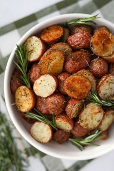 a white bowl filled with cooked potatoes and rosemary sprigs on top of a checkered tablecloth