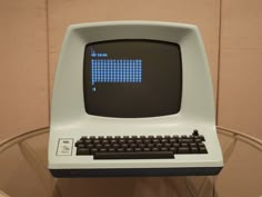 an old computer sitting on top of a glass table in front of a beige wall