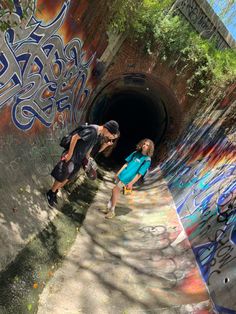 two people standing in front of a tunnel with graffiti on it