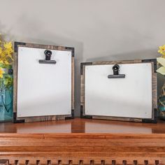 two wooden frames with clipboards attached to them sitting on a shelf next to flowers