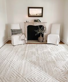 a white living room with two chairs and a rug on the floor in front of a fireplace