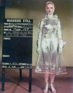 a woman standing in front of a sign wearing a silver dress and matching heels with her hands on her hips