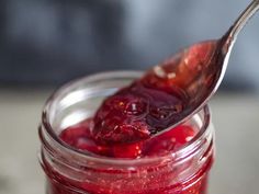 a spoon full of jam on top of a jar filled with jelly and cranberry sauce