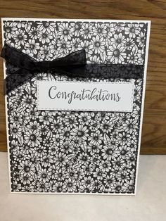 a congratulations card with black and white flowers on it, tied with a black ribbon