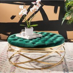 a round coffee table with a green velvet cushion and gold metal frame, sitting on a rug in front of a wall