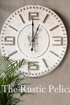 a large white clock mounted to the side of a wall next to a potted plant