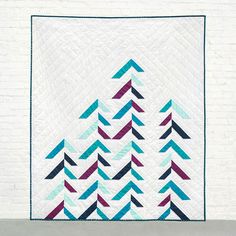 a quilted wall hanging on the side of a white brick wall with blue, purple and green arrows