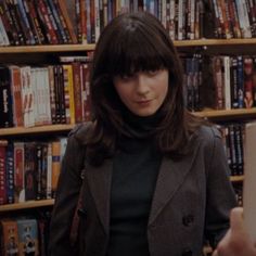 a woman standing in front of a bookshelf holding an electronic device and looking at the camera