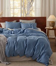 a bed with blue sheets and pillows in front of a window, next to a lamp