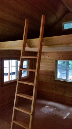 a ladder is in the middle of a room with wood paneling and two windows