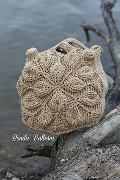 a crocheted bag sitting on top of a tree branch next to the water