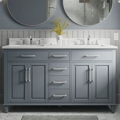 two round mirrors are above the double sinks in this gray bathroom with white tile flooring