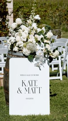 a wooden barrel filled with white flowers and greenery next to a sign that says kate & matt