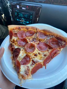 a slice of pepperoni pizza on a paper plate in someone's hand,