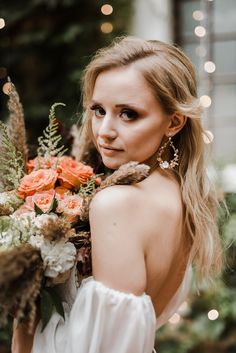 a beautiful woman holding a bouquet of flowers in her hand and looking at the camera