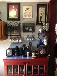 there is a red cabinet with coffee cups on it and pictures above the door to the kitchen