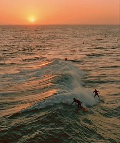 two surfers are riding the waves in the ocean as the sun sets behind them