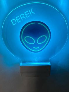 an alien light up sign with the word derek on it's face in front of a blue background