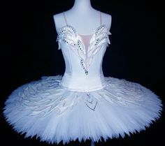 a white tutu with feathers and beads on the top is sitting on a mannequin