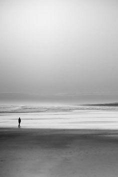 two people are walking on the beach in black and white