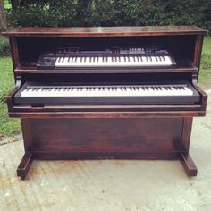 an old piano is sitting outside on the sidewalk in front of some grass and trees