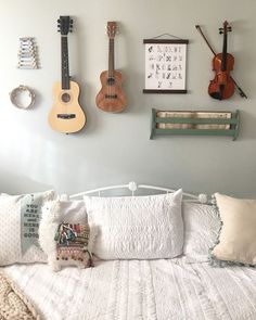 a white bed topped with lots of pillows and guitars hanging on the wall above it