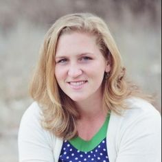 a woman with blonde hair wearing a white cardigan and blue polka dot top smiling at the camera