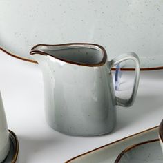 a white pitcher sitting on top of a table next to other plates and cups with saucers