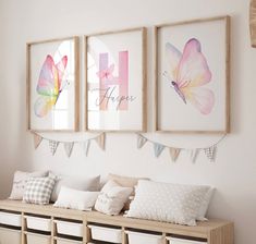 three framed pictures hang on the wall above a bench with pillows and baskets underneath it