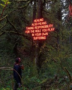 a man standing in the woods next to a neon sign