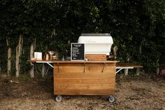 an outdoor bbq grill on wheels in front of some trees and bushes with a chalkboard sign