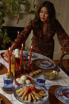 a woman standing over a table filled with plates and bowls full of food next to candles