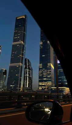 the city skyline is lit up at night as seen from inside a car's side view mirror