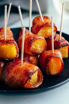 bacon wrapped pineapples on a black plate with toothpicks in the middle