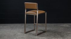 a tan leather and metal bar stool against a black brick wall in an empty room