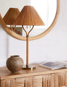 a table lamp sitting on top of a wooden dresser next to a mirror and book