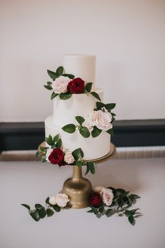 a three tiered white wedding cake with red and pink flowers on top is surrounded by greenery