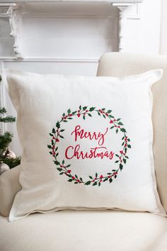 a christmas pillow sitting on top of a couch next to a fire place with a wreath