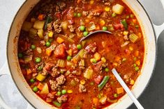 a pot filled with meat and vegetables on top of a table next to a spoon