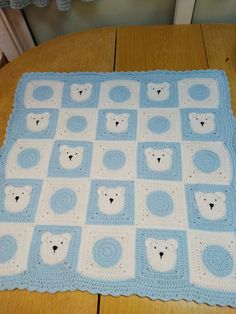 a blue and white crocheted baby blanket with polar bears on the top, sitting on a wooden table