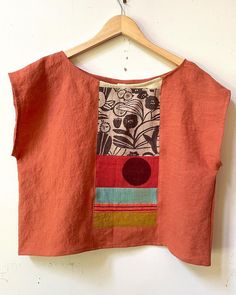 an orange top hanging on a wooden hanger next to a white wall with a black and red flower design