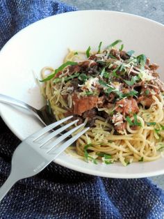 a white bowl filled with pasta and meat on top of a blue towel next to a fork