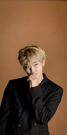 a young man in a black suit posing for a photo with his hand on his chin